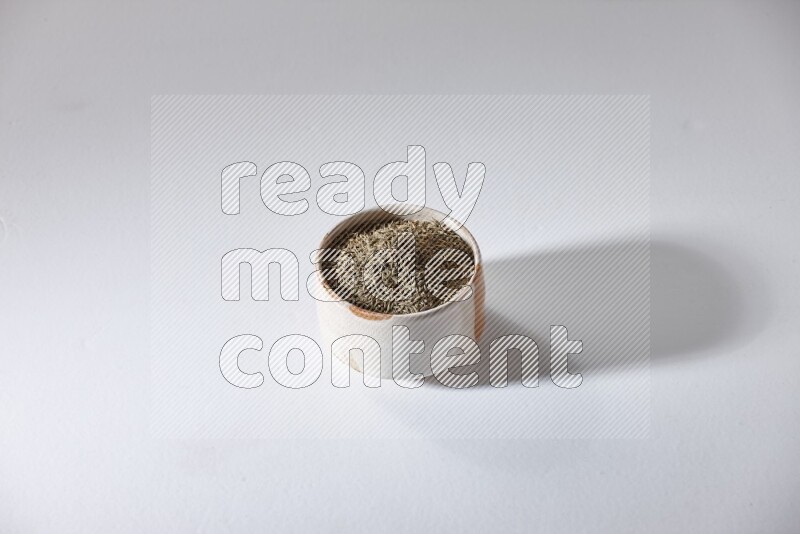 A beige bowl full of cumin seeds on a white flooring