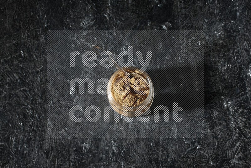 وعاء زجاجي للتوابل وملعقة معدنية ممتلئان ببودرة بهار الفلفل الحلو على خلفية سوداء