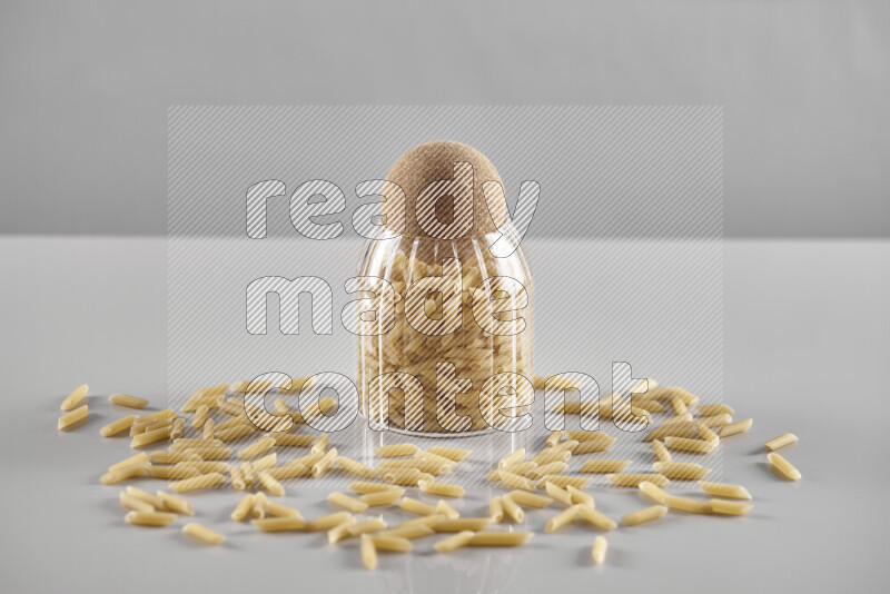 Raw pasta in a glass jar on light grey background
