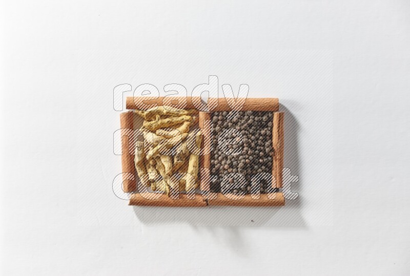 مربعان من أعواد القرفة ممتلئان بحبوب الفلفل الأسود وأصابع الكركم علي خلفية بيضاء