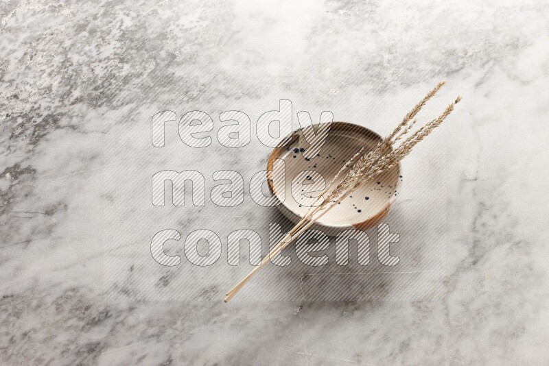 Wheat stalks on multicolored pottery bowl on grey marble background
