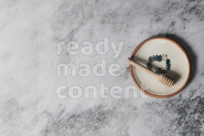 Decorative pottery plate with wooden honey dipper in it on grey marble background