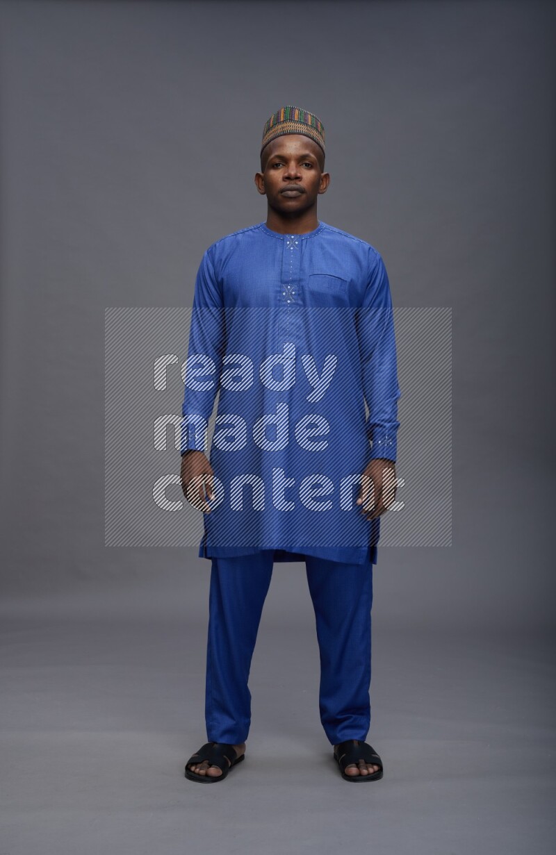 Man wearing Nigerian outfit standing interacting with the camera on gray background