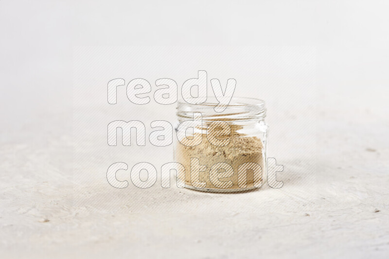 A glass jar full of ground ginger powder on white background