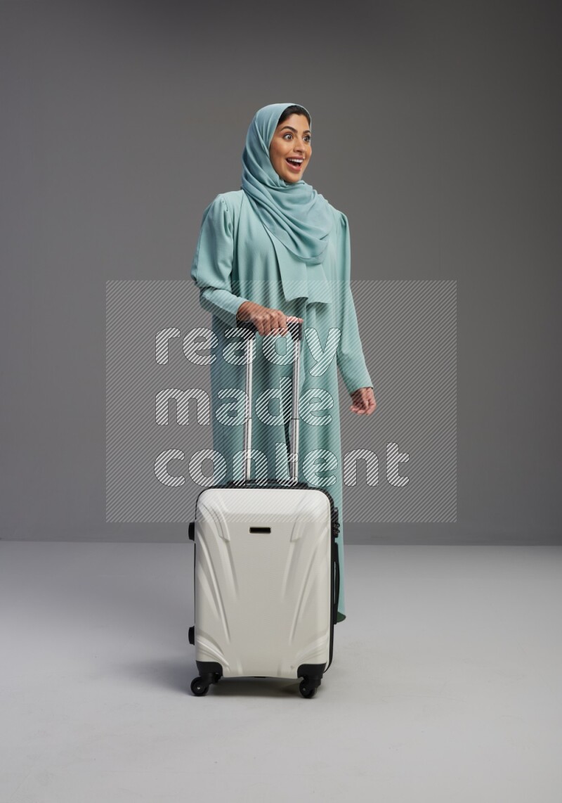 Saudi Woman wearing Abaya standing holding Travel bag on Gray background