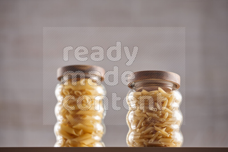 Raw pasta in glass jars on beige background