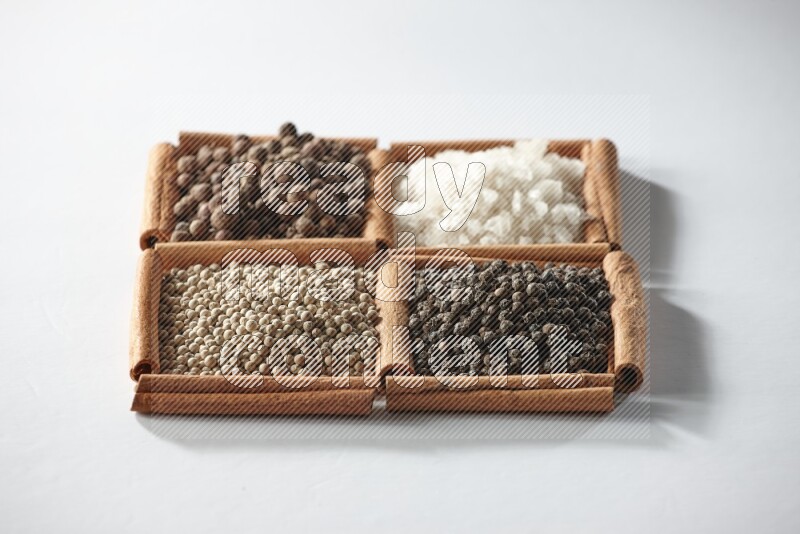 4 مربعات من أعواد القرفة ممتلئة ببهار الفلفل الحلو والملح الأبيض والفلفل الأبيض والفلفل الأسود على أرضية بيضاء