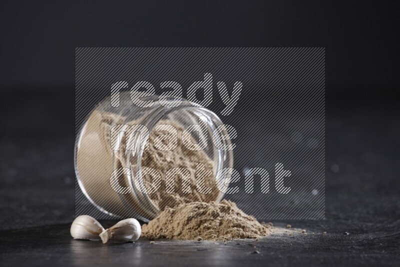 A glass jar full of garlic powder flipped over with the powder came out on a textured black flooring
