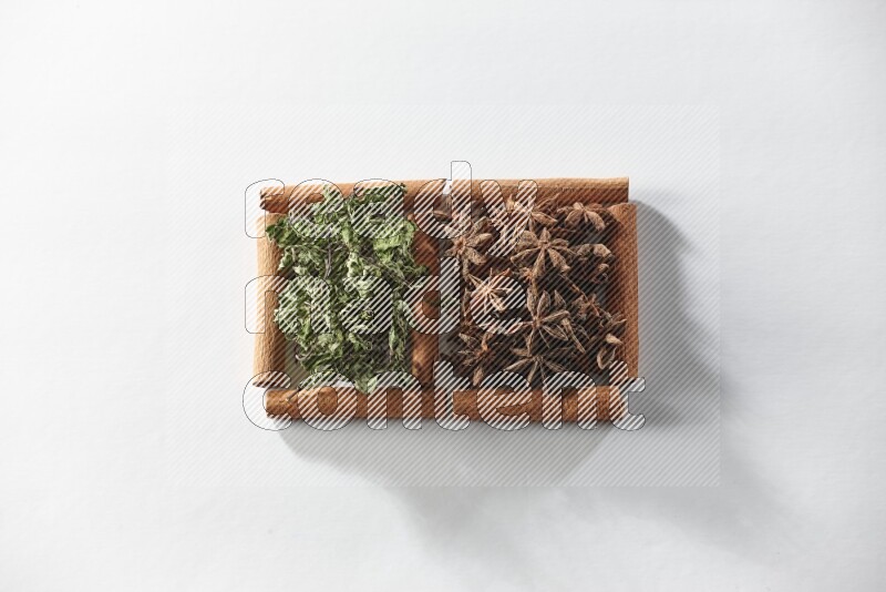 2 squares of cinnamon sticks full of star anise and dried mint leaves on white flooring