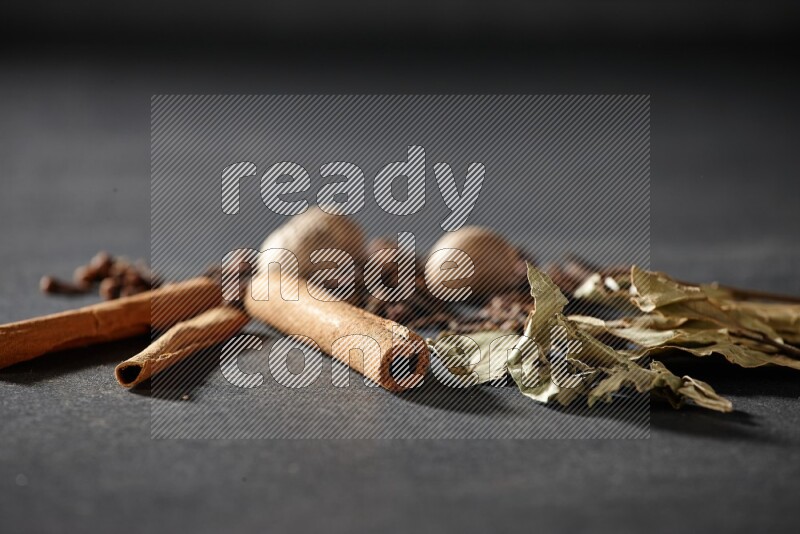 Cloves, ginger, bay laurel and cinnamon sticks on black flooring