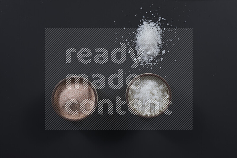 2 pottery bowls one is filled with himalayan salt and the other with white salt on black background