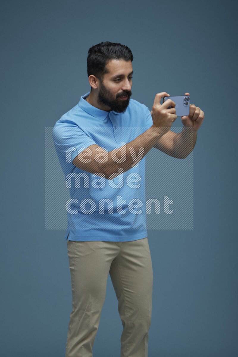 Man taking a picture with his phone  in a blue background wearing a Blue shirt