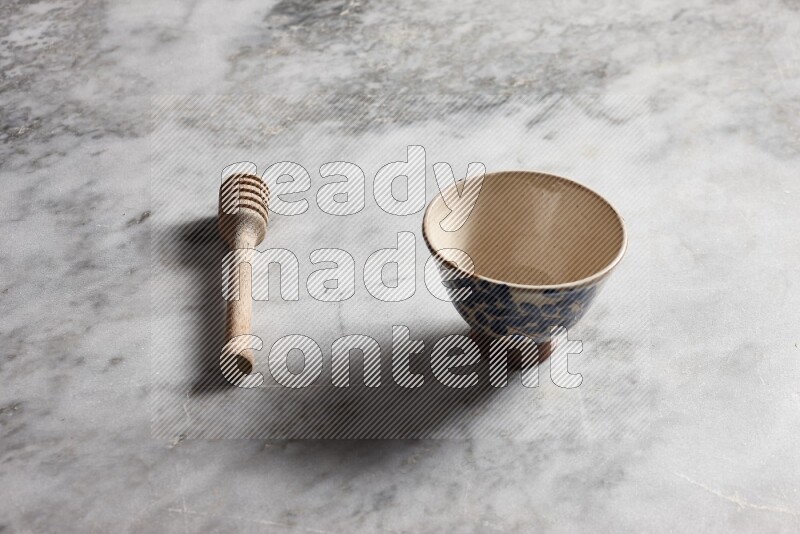 Decorative pottery bowl with wooden honey dipper on the side on grey marble background