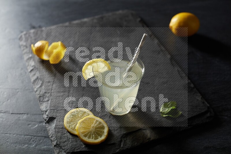 A glass of lemon juice with a straw on black background