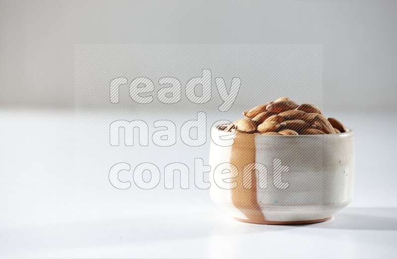 A beige ceramic bowl full of peeled almonds on a white background in different angles