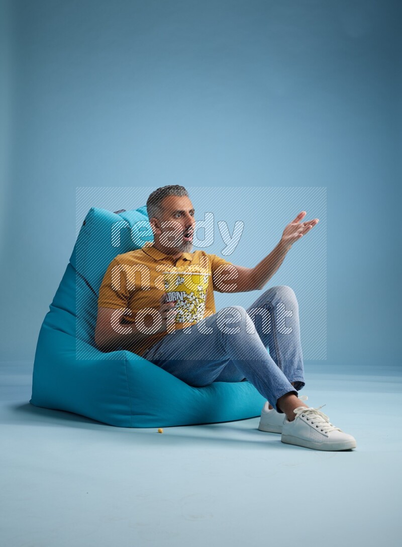 A man sitting on a blue beanbag and eating popcorn
