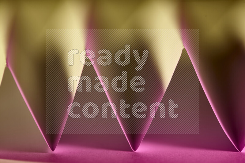 A close-up abstract image showing sharp geometric paper folds in pink gradients and warm tones