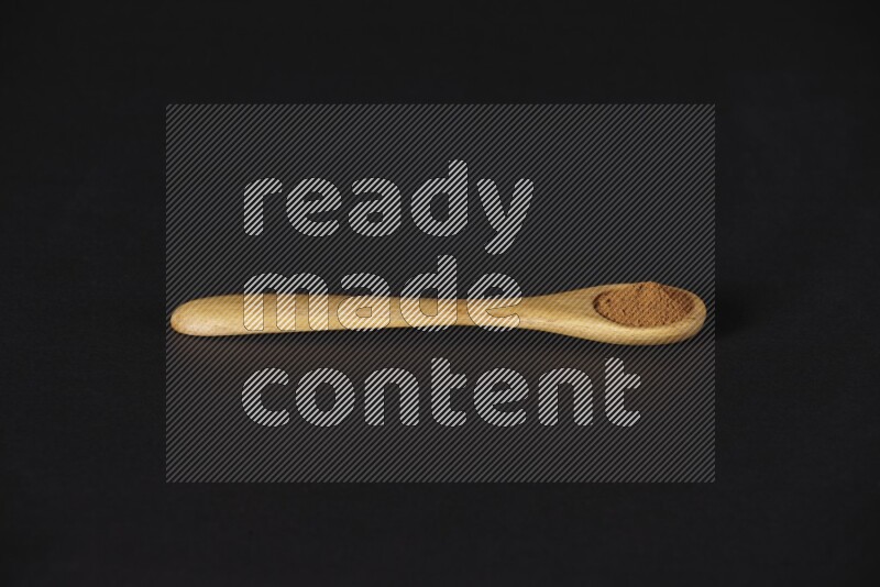Cinnamon powder in a wooden spoon on a black background