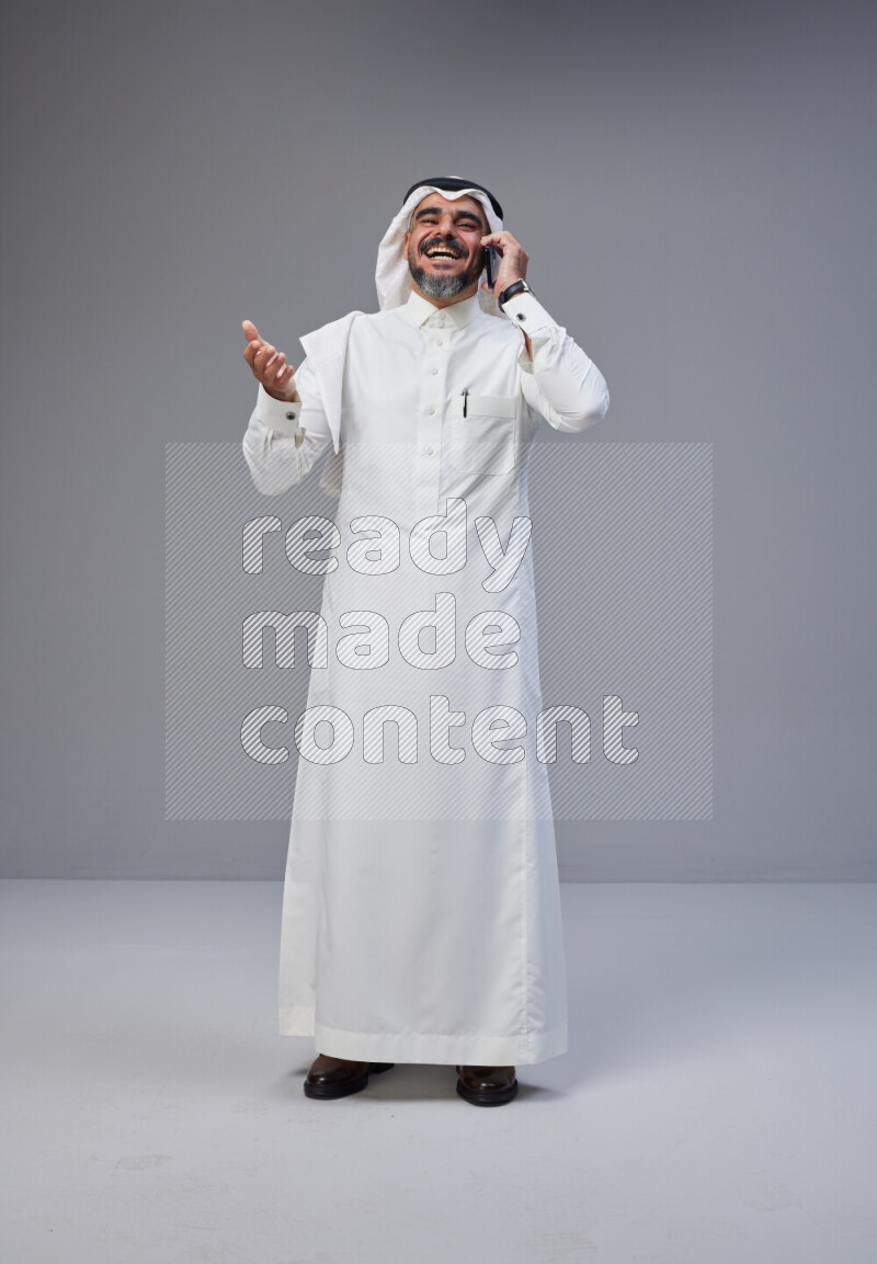 Saudi man Wearing Thob and white Shomag standing talking on phone on Gray background