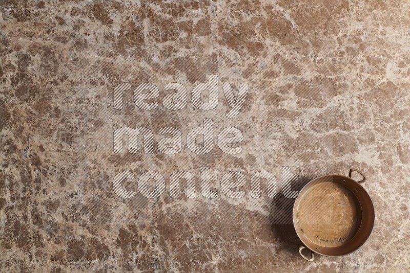 A small copper pan on beige marble background
