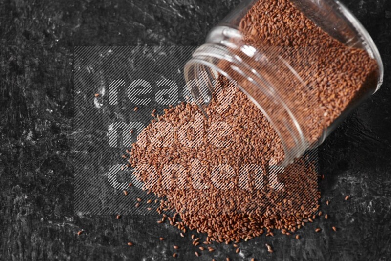A glass jar full of garden cress seeds flipped and seeds spread out on a textured black flooring