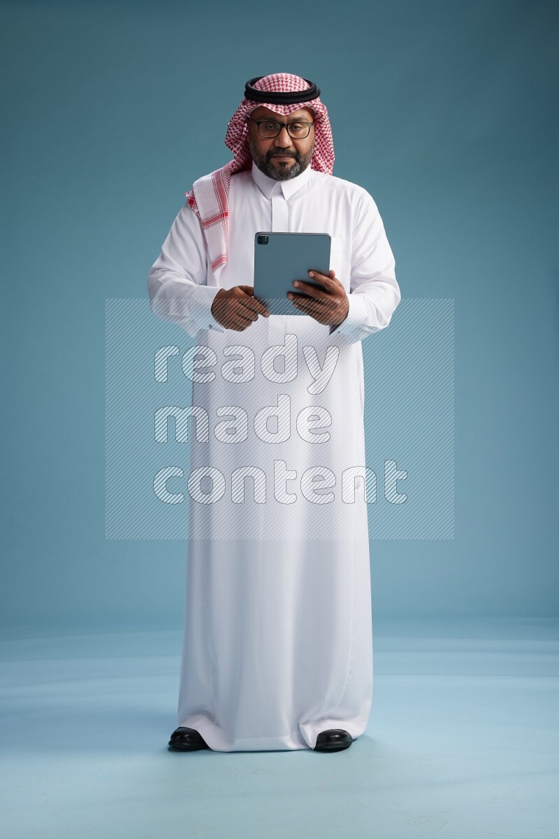 Saudi Man with shimag Standing holding a tablet on blue background