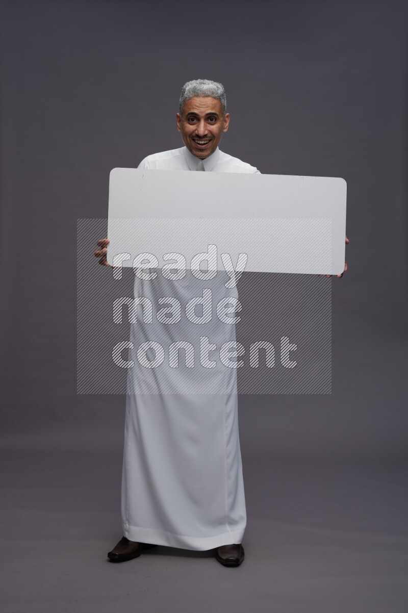 Saudi man wearing thob standing holding board on gray background