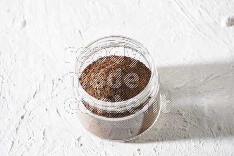 A glass jar full of cloves powder on a textured white flooring
