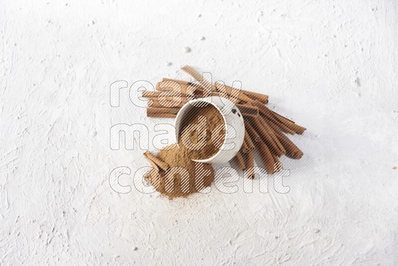 Ceramic beige bowl over filled with cinnamon powder and cinnamon sticks around the bowl on a textured white background in different angles
