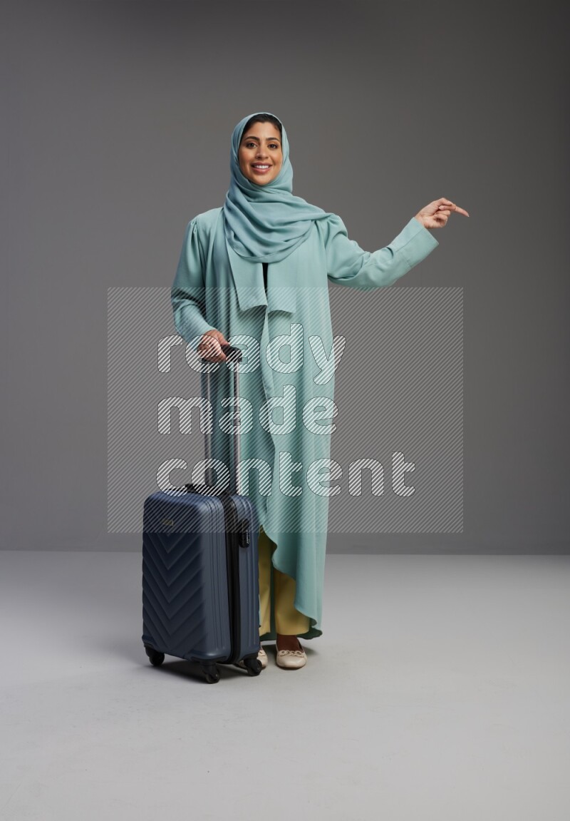 Saudi Woman wearing Abaya standing holding Travel bag on Gray background