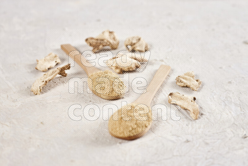 Two wooden spoons full of ground ginger powder on white background