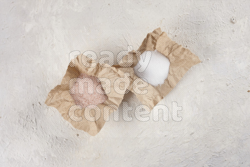 2 crumpled pieces of paper full of pink himalayan salt and white salt on white background
