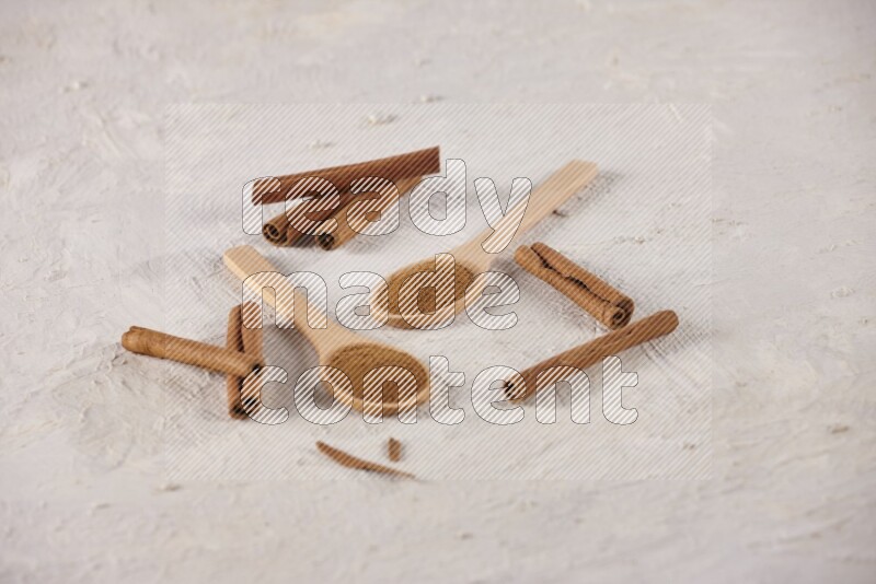 Two wooden spoons full of cinnamon powder with cinnamon sticks on white background