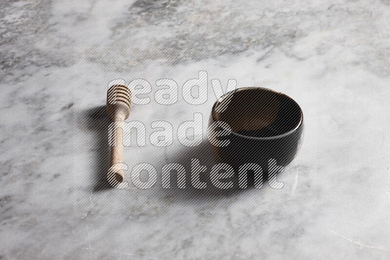 Multicolored pottery bowl with wooden honey dipper on the side on grey marble background