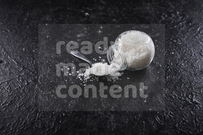 وعاء زجاجي ممتلئ بملح البحر الخشن على خلفية سوداء