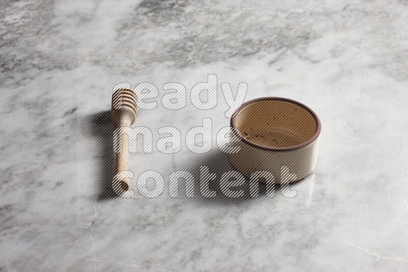 Beige pottery oven bowl with wooden honey dipper on the side on grey marble background