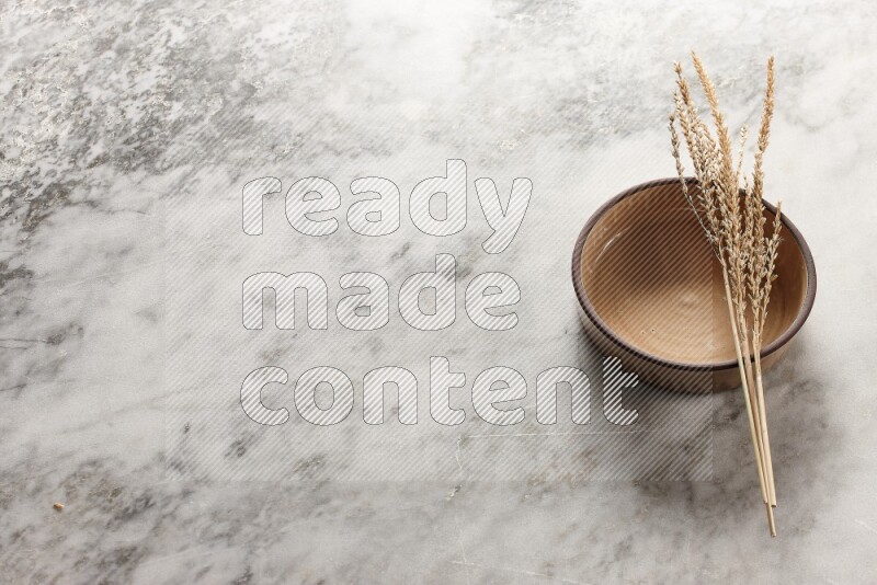 Wheat stalks on beige pottery oven bowl on grey marble background
