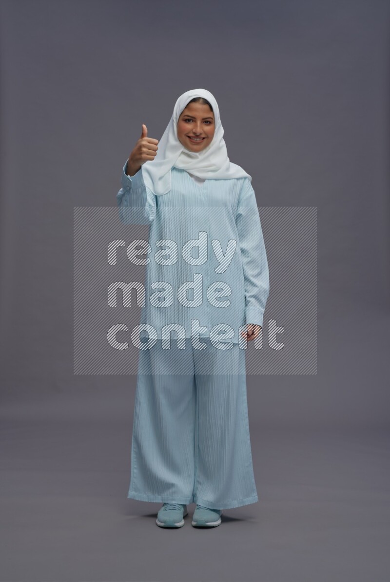 Saudi woman wearing hijab clothes standing interacting with the camera on gray background