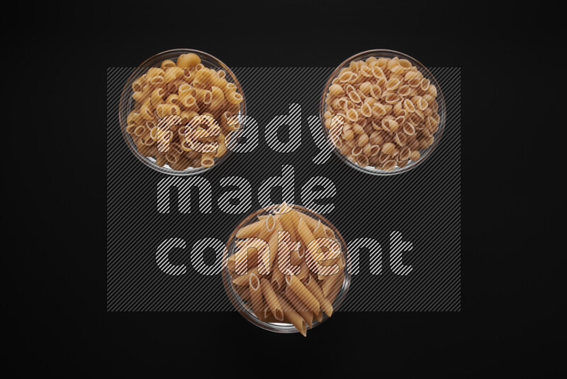 Different pasta types in glass bowls on black background