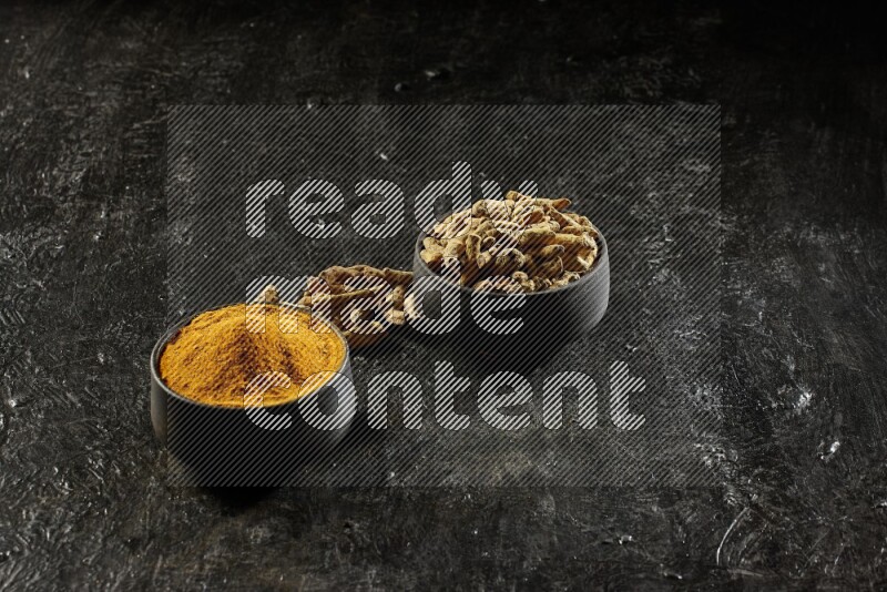 وعاءان من الفخار باللون الأسود، أحدهما ممتلئ ببودرة الكركم والآخر ممتلئ بأصابع كاملة من الكركم المجفف على خلفية سوداء