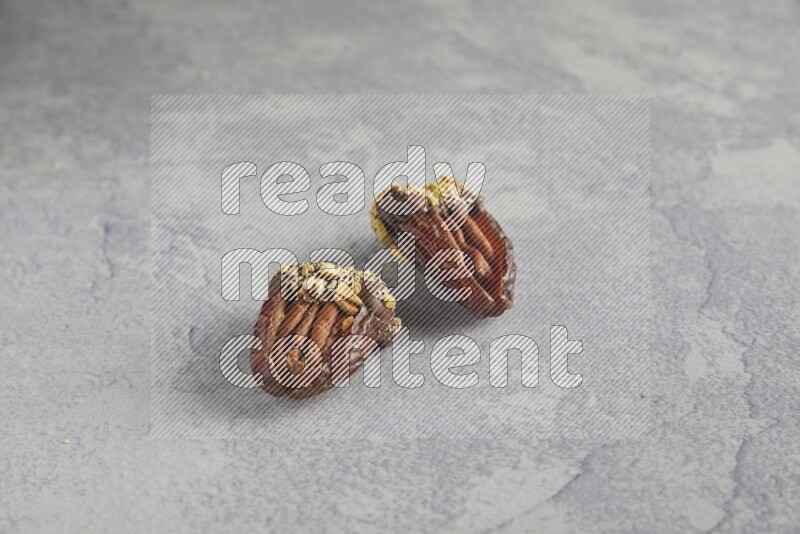 Two pecan stuffed dates covered with Dark chocolate and chopped pistachios on alight grey background