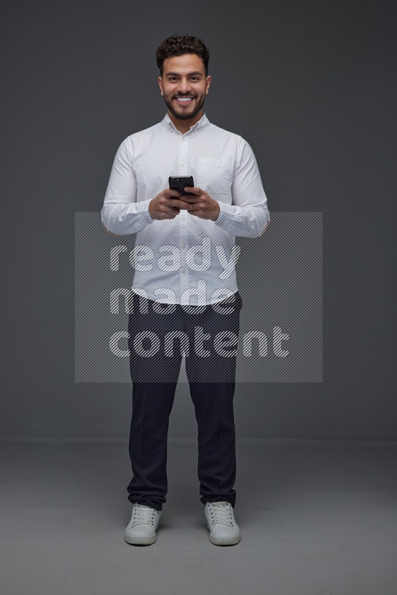 A man wearing smart casual standing and using his phone eye level on a gray background