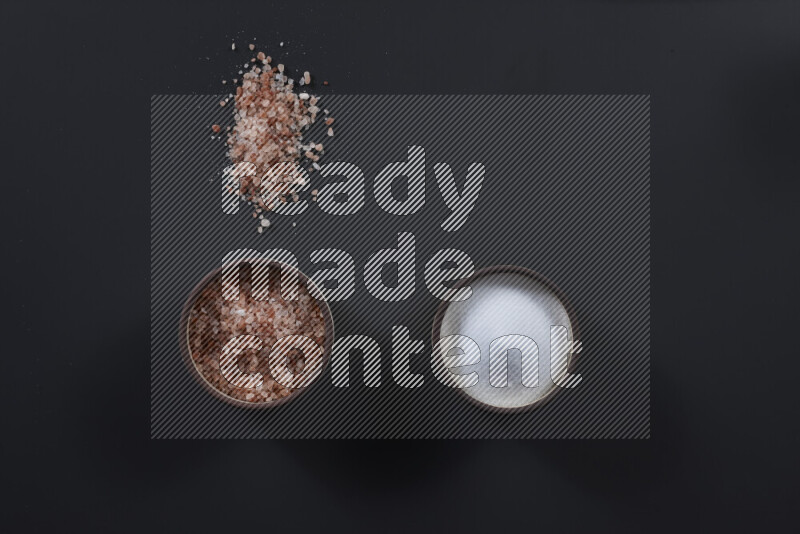 2 pottery bowls one is filled with himalayan salt and the other with white salt on black background