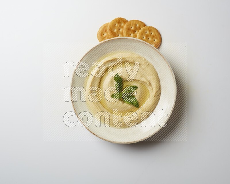 Hummus in a pottry plate garnished with mint  on a white background