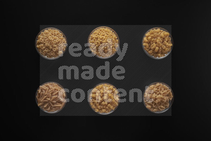 Different pasta types in 6 glass bowls on black background