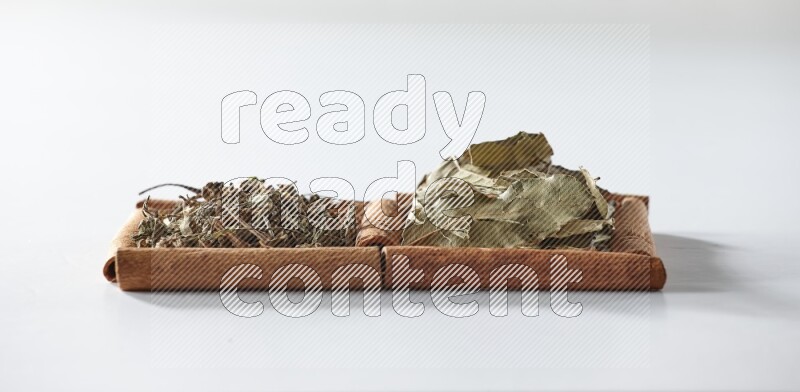 مربعان من أعواد القرفة ممتلئان بالريحان المجفف وأوراق الغار علي خلفية بيضاء