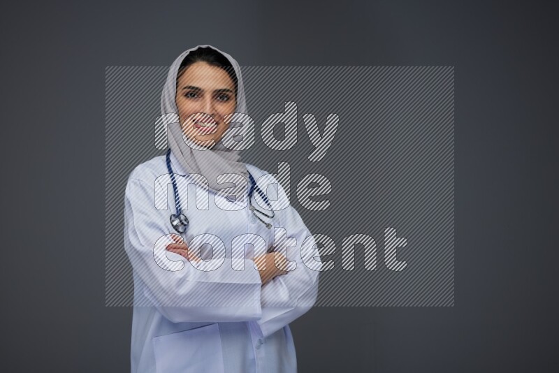 A female doctor wearing a light gray head scarf standing on grey background.