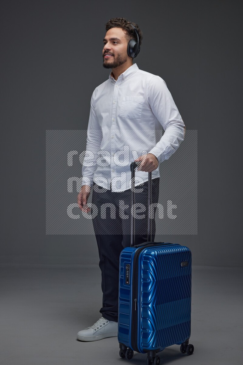 A man Posing with a carry-on with headsets  Wearing a White shirt on a grey background