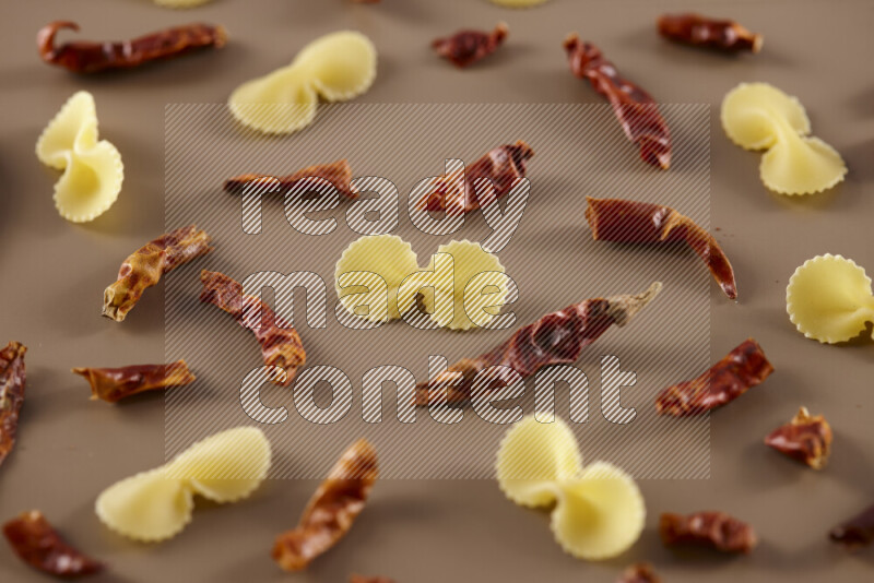 Raw pasta with different ingredients such as cherry tomatoes, garlic, onions, red chilis, black pepper, white pepper, bay laurel leaves, rosemary and cardamom on beige background