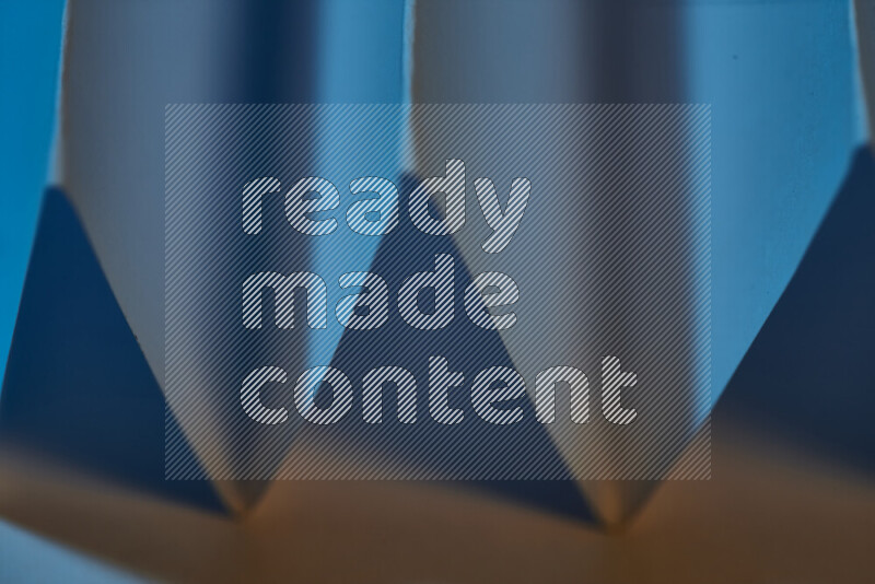 A close-up abstract image showing sharp geometric paper folds in blue gradients and warm tones